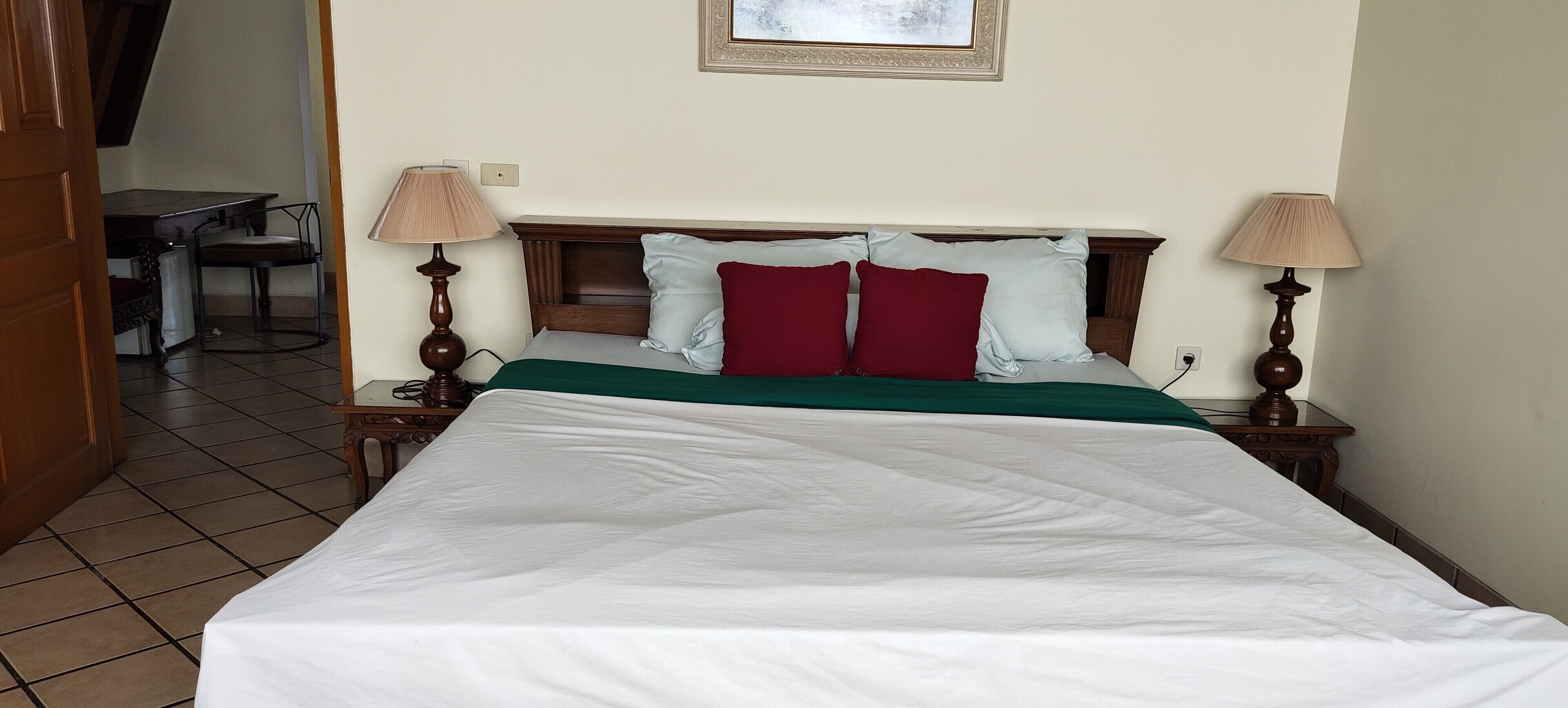 A neatly made bed with a green bedspread and white sheets, flanked by two bedside lamps.
