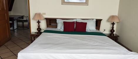 A neatly made bed with a green bedspread and white sheets, flanked by two bedside lamps.