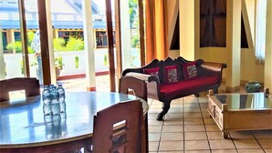 A dining area with a table, chairs, a sofa, and a glass-top coffee table. - OBC Villa (Bandung)