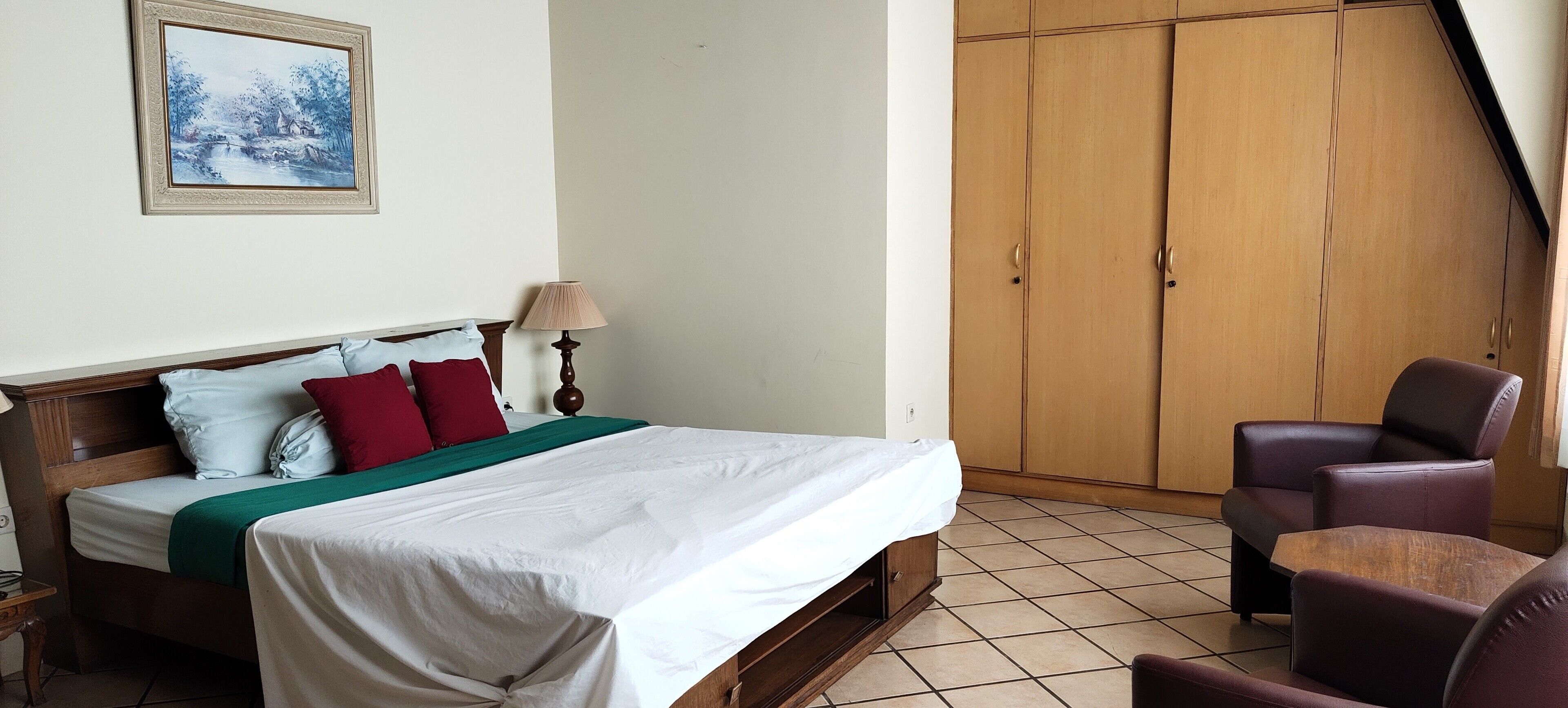 A bedroom with a bed, a nightstand, a lamp, a chair, and a wardrobe.
