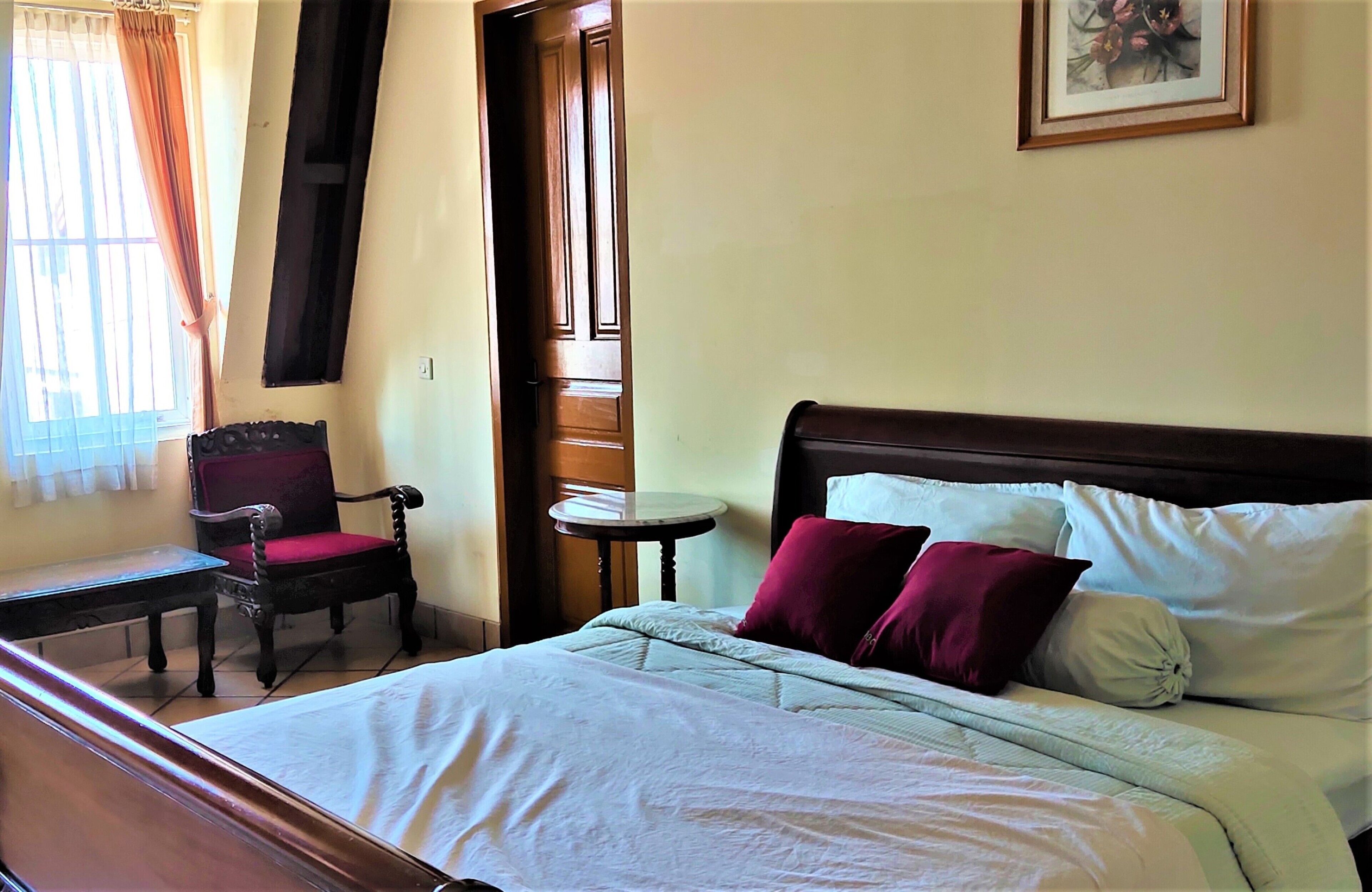 A hotel room with a bed, a chair, a small table, and a window with curtains.