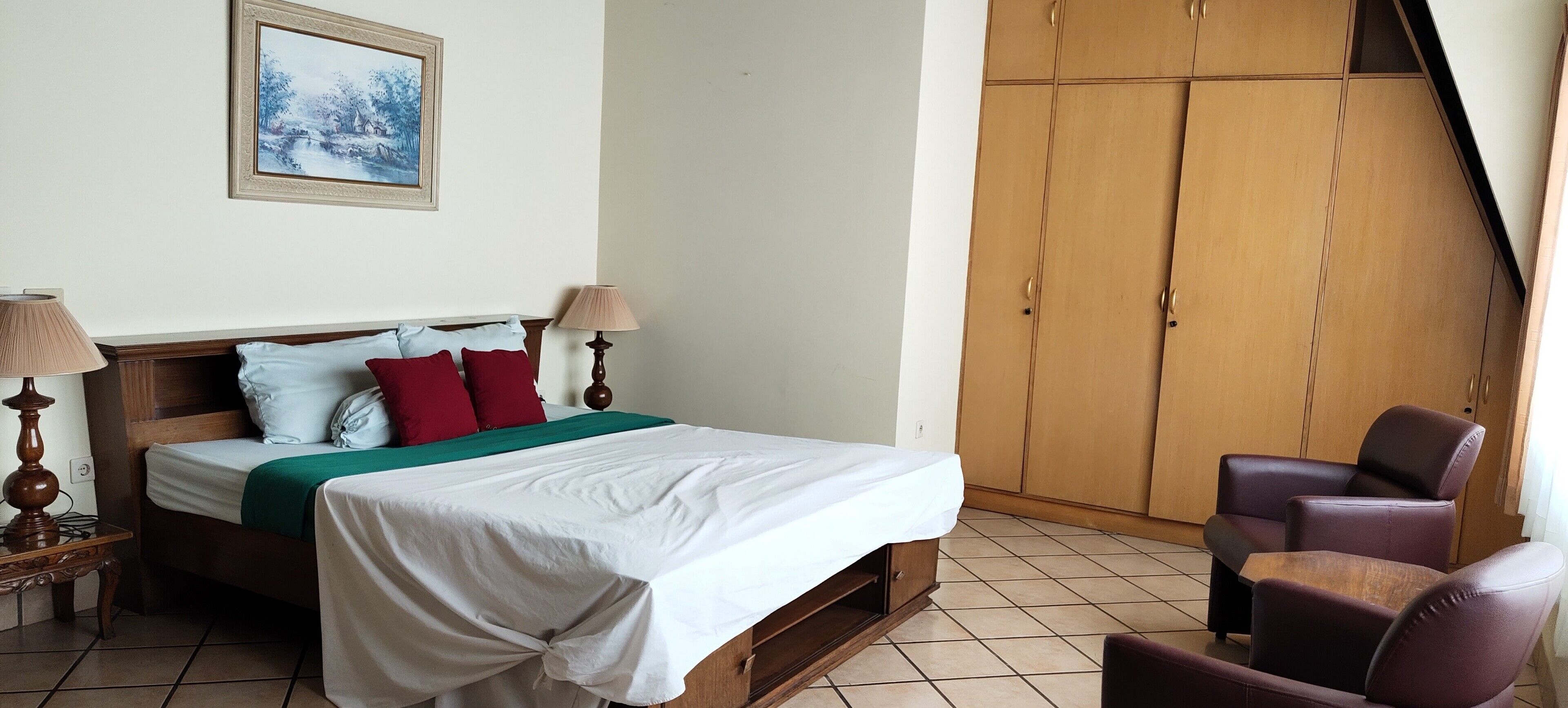 Un dormitorio con una cama, dos lámparas de noche, un armario de madera y una silla.