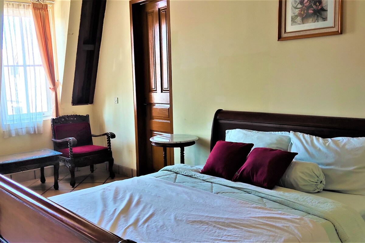 A hotel room with a bed, a chair, a small table, and a window with curtains.