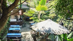 An outdoor seating area with tables and chairs, surrounded by lush greenery and a large umbrella. - OBC Villa (Bandung)