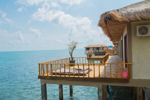 An overwater bungalow with a thatched roof, a balcony with a railing, and a view of the sea.