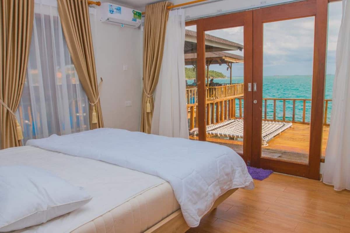 Een slaapkamer met een bed, gordijnen en uitzicht op de oceaan door een schuifdeur.