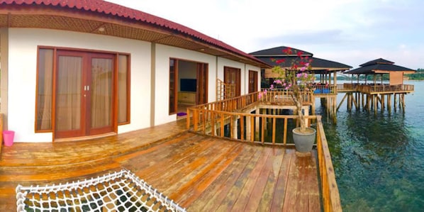 A wooden deck with a netted area, wooden railings, and a view of water and overwater bungalows.