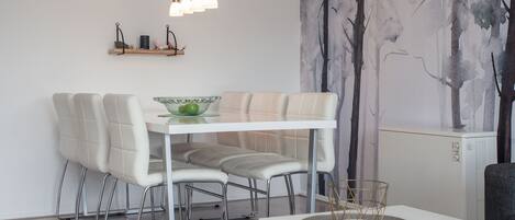 A modern dining area with a white table and chairs, a hanging light fixture, and a wall mural.