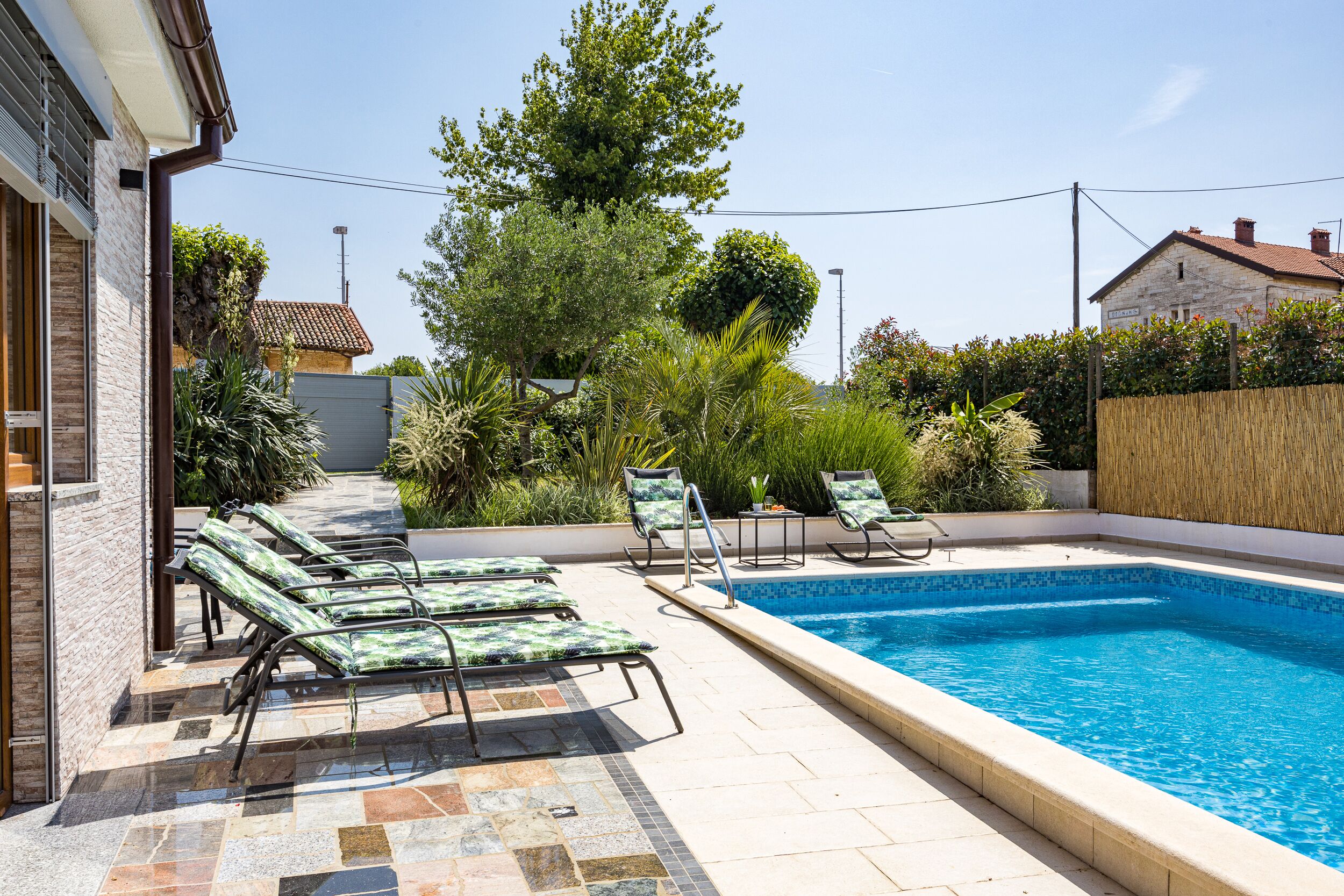 Ein Swimmingpool mit Liegestühlen, umgeben von Grünpflanzen und einer Steinmauer.