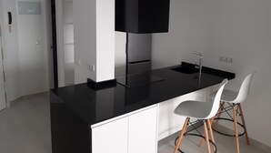 Cozinha moderna com bancada preta, armários brancos e dois bancos altos brancos.
