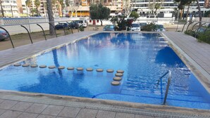 Uma piscina retangular com um deck ladrilhado, cercada por uma cerca baixa e um guarda-corpo metálico na borda.