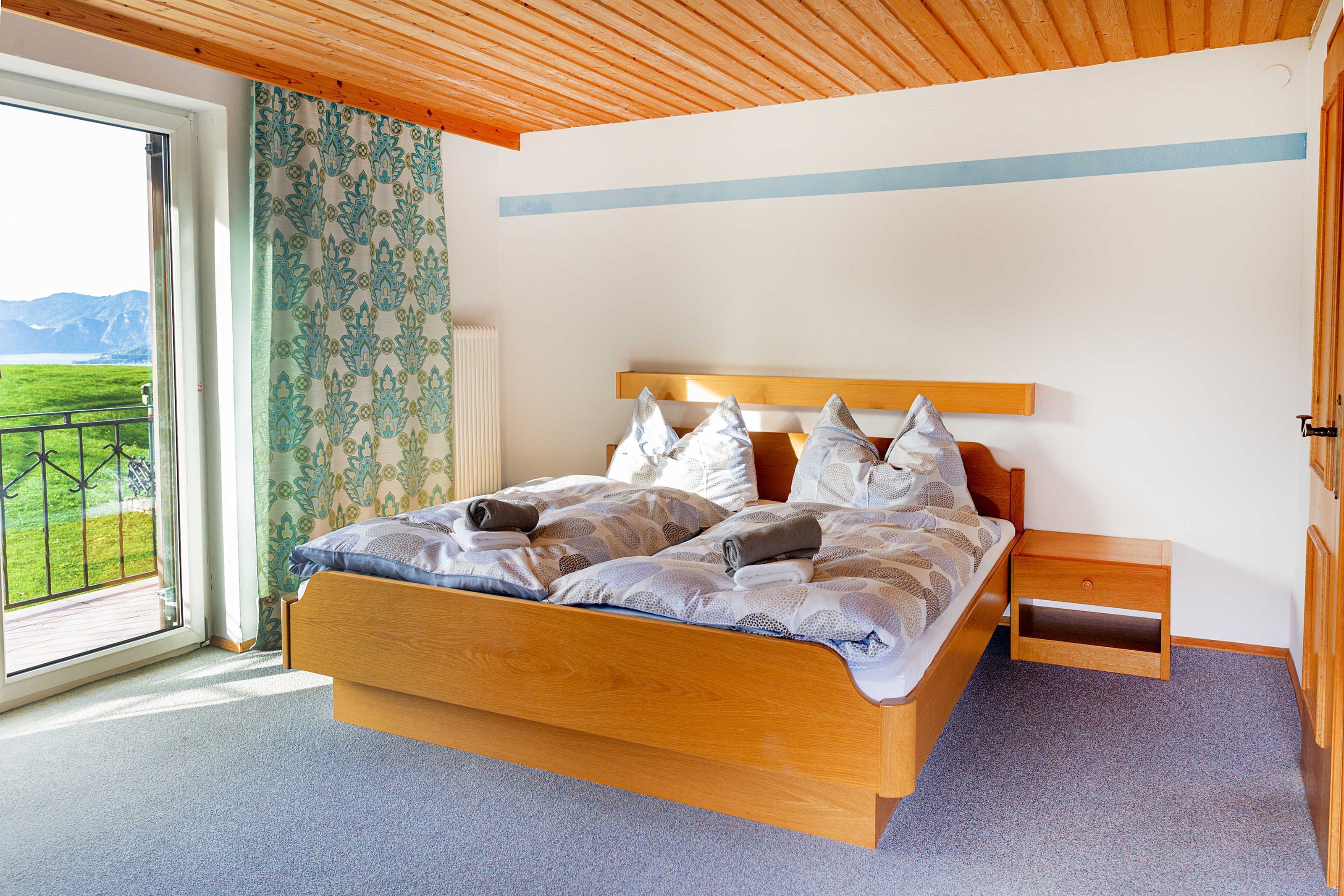 Une chambre à coucher avec un lit en bois, une table de chevet et une vue sur un paysage verdoyant par la fenêtre.