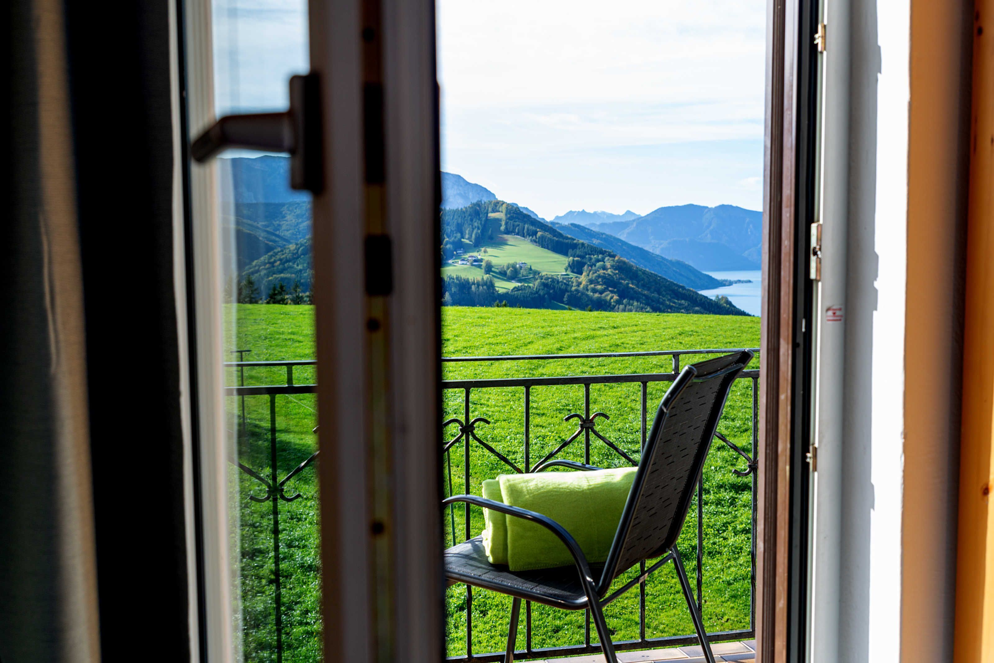 Ein Balkon mit Stuhl und Kissen mit Blick auf eine grüne Landschaft und Berge.