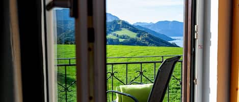 Un balcón con una silla y un cojín, con vistas a un paisaje verde y montañas.