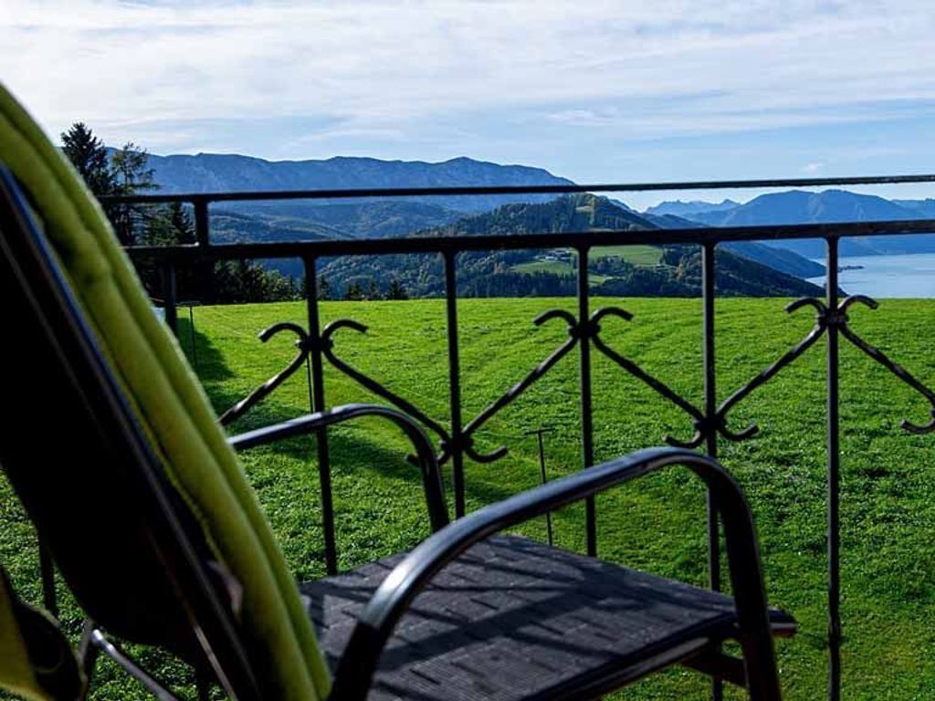 Een balkon met een metalen hekwerk, met uitzicht op een grasveld en verre bergen.