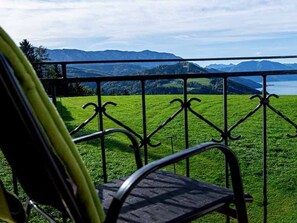 A balcony with a metal railing overlooking a grassy field and distant mountains.
