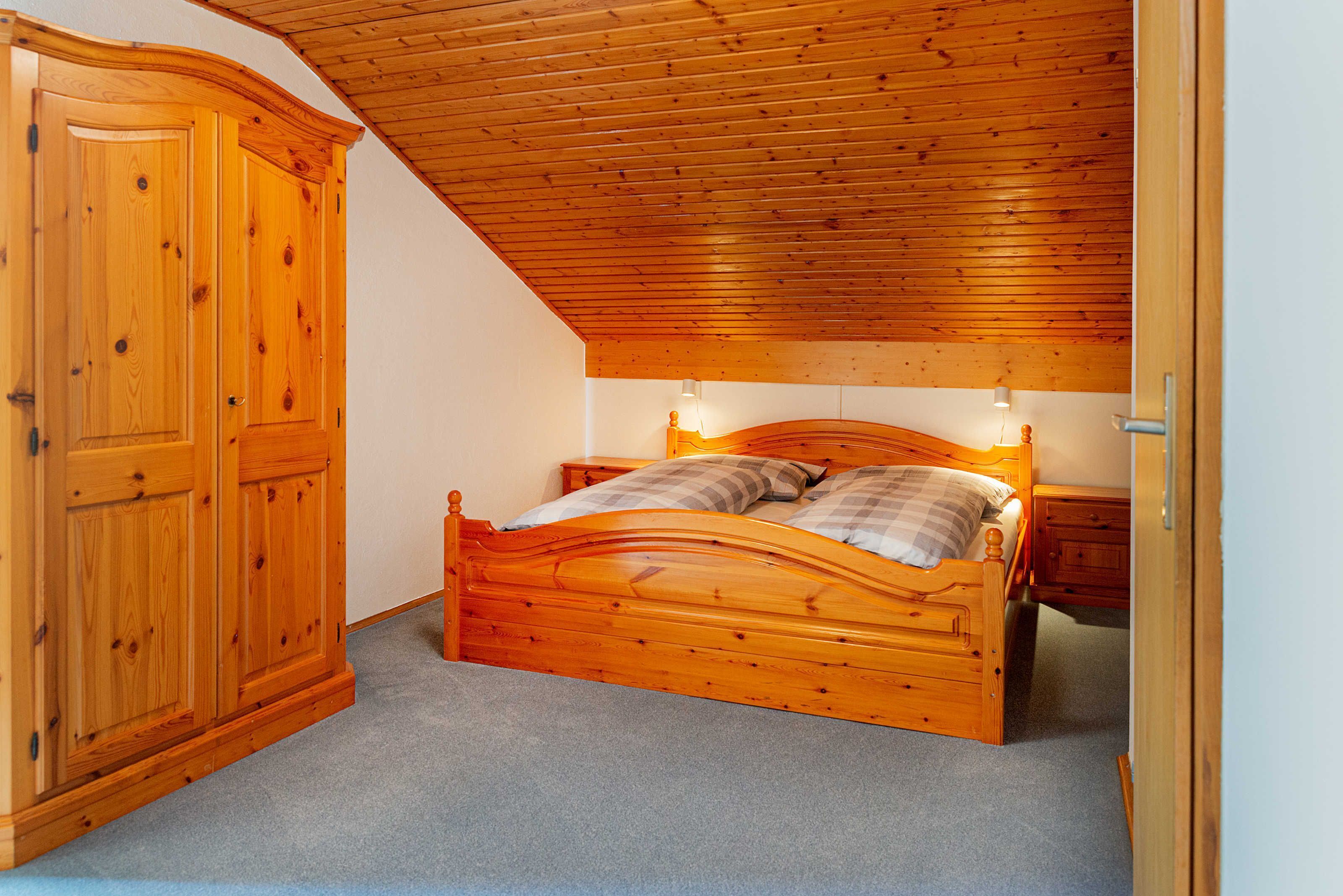 Une chambre à coucher avec un lit en bois, une armoire et un plafond en pente.