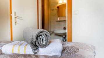 Un lit avec des serviettes enroulées et un coussin à motifs, une porte donnant sur une salle de bain, et un miroir qui reflète la salle de bain.