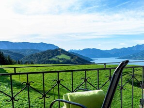 Ein Balkon mit Metallgeländer, einem grünen Stuhl und Blick auf einen See, der von Bergen umgeben ist.
