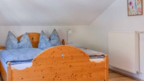 Ein hölzernes Bett mit geschwungener Kopfteil, ein weißer Heizkörper und eine Wandleuchte.