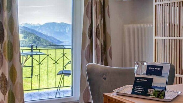 Une chambre avec vue sur les montagnes, un ordinateur portable posé sur une table et un panneau d’accueil.