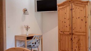 Une chambre à coucher avec un lit en bois, un bureau avec une chaise, une armoire et un téléviseur fixé au mur.