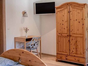 A bedroom with a wooden bed, a desk with a chair, a wardrobe, and a TV mounted on the wall. - Doppelzimmer 8 - Brandnerhof (Gahberg)