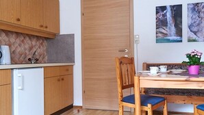 Une cuisine de taille réduite, avec des meubles de rangement en bois, un réfrigérateur blanc, une table à manger avec des chaises et une porte.