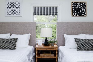 A bedroom with two beds, a nightstand with a lamp, a small plant, and artwork on the walls.