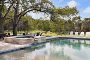 A swimming pool with a stone deck, surrounded by trees and outdoor seating.