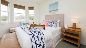 Quarto com cama, mesa de cabeceira e vista para o exterior por grandes janelas.