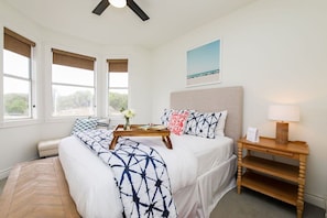 A bedroom with a bed, bedside table, and a view of the outdoors through large windows. - Hill Country Escape | Pool, Hot Tub & Sleeps 25 (Austin)