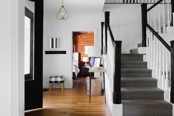 A staircase with a herringbone pattern carpet, a black and white railing, and a wooden floor leading to a bedroom with a bed and a nightstand.