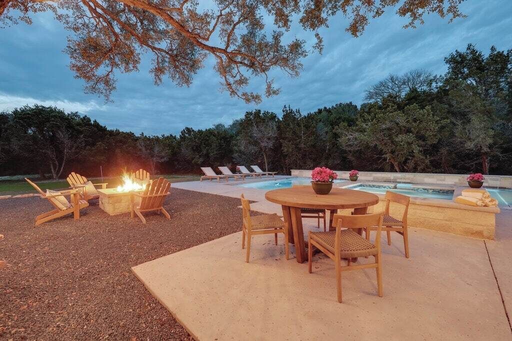 Een terras buiten met een vuurkuil, lounge fauteuils en een zwembad.