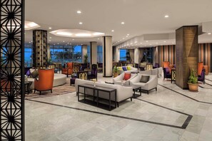 Un lobby amplio con muebles modernos, ventanas grandes y un panel decorativo en la pared.