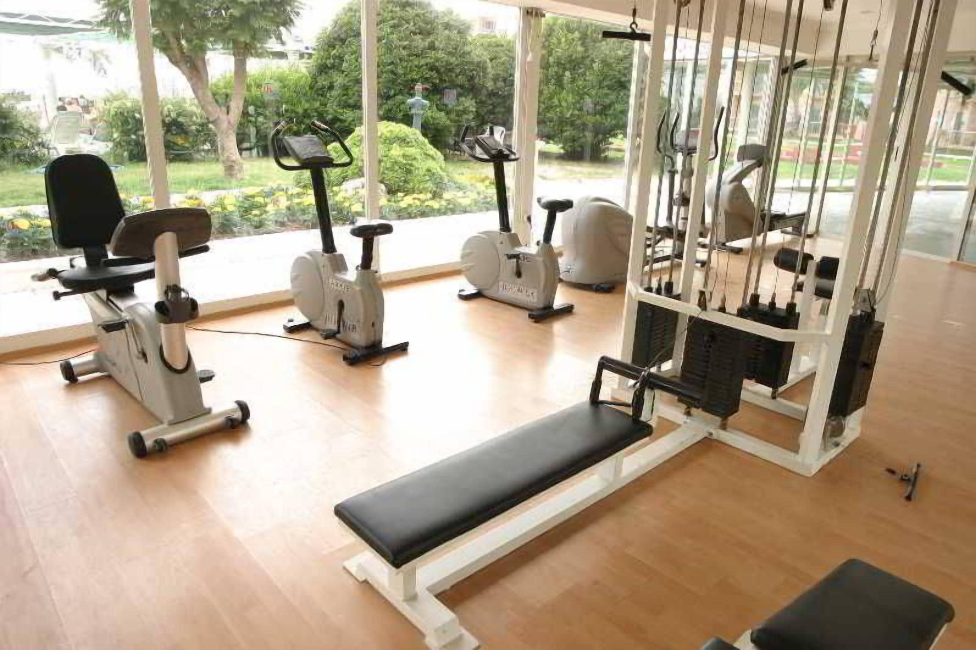 Un gimnasio con equipo de ejercicio, una banca y ventanas amplias con vistas a zonas verdes.