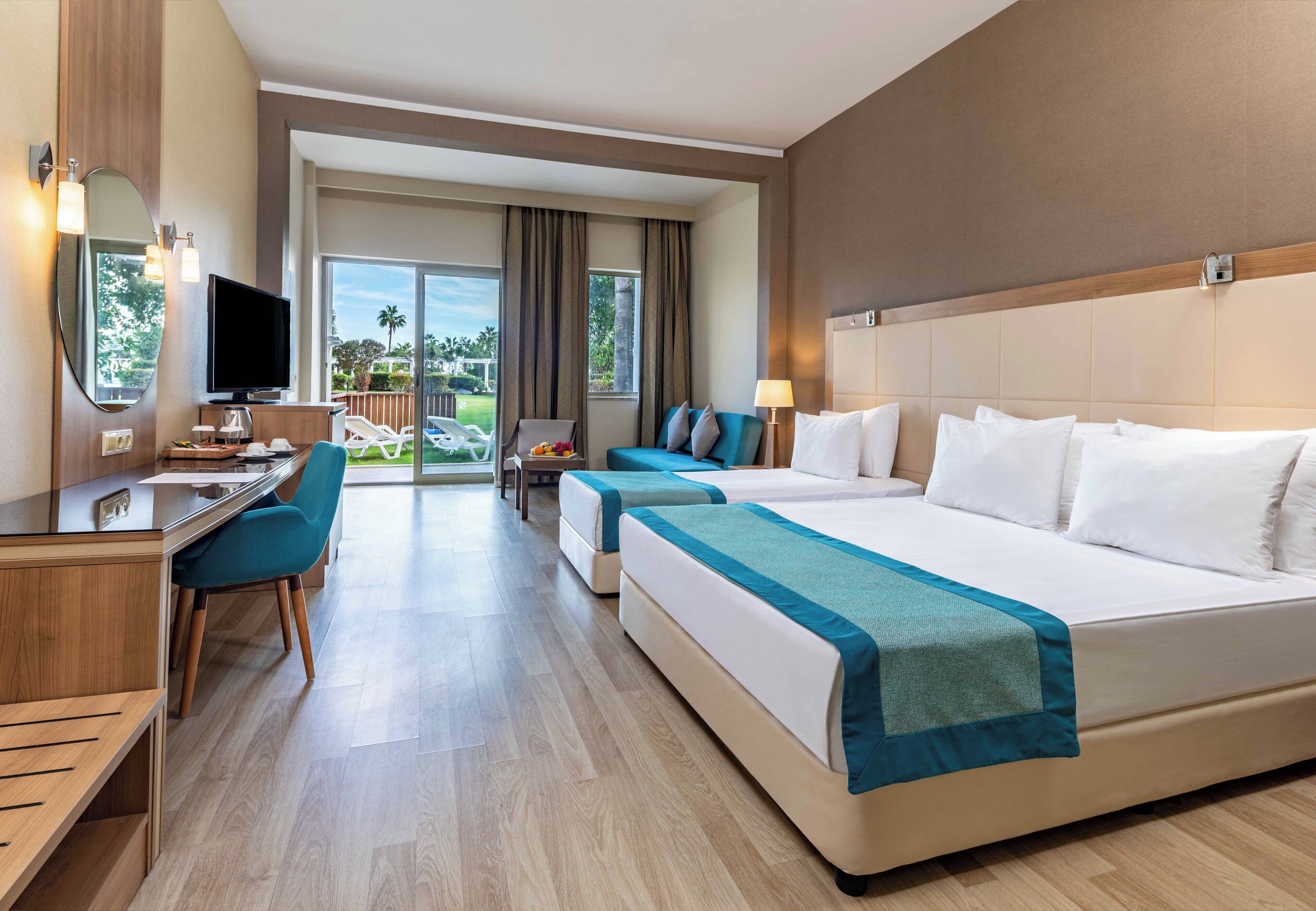 A hotel room with a bed, desk, chair, TV, and a view of the outdoors.