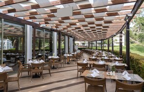 An outdoor dining area with wooden tables and wicker chairs, covered by a wooden ceiling with a checkered pattern. - Kaya Side Hotel (Manavgat)