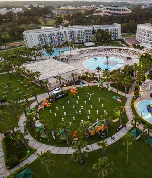 Un resort con varias piscinas, palmeras y un césped central con una estatua.