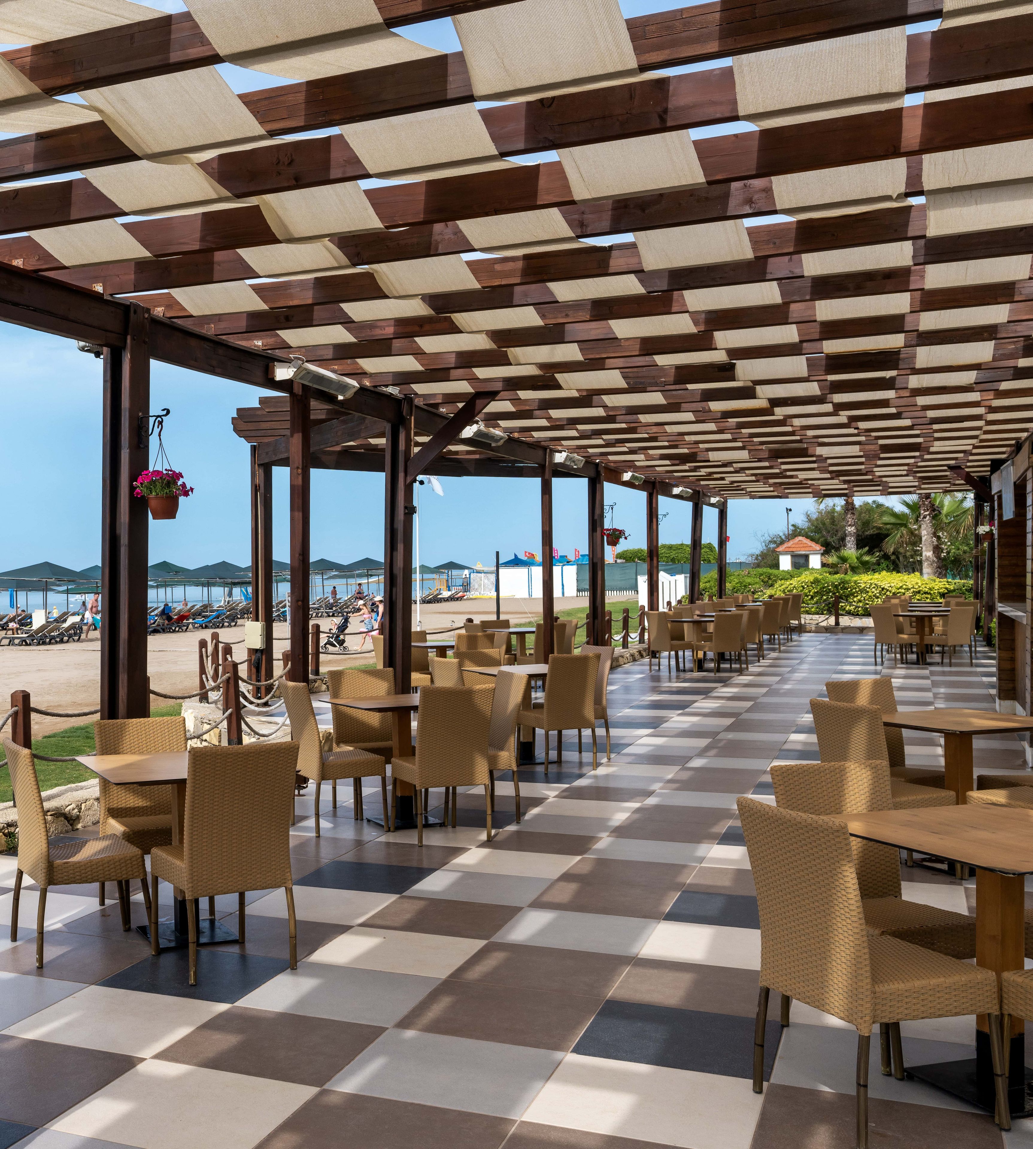 A covered outdoor seating area with checkered flooring and wicker chairs, overlooking a beach.