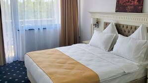 A hotel room with a large bed, a white headboard, a painting on the wall, and a window with curtains. - Hotel Terra (Neptun)