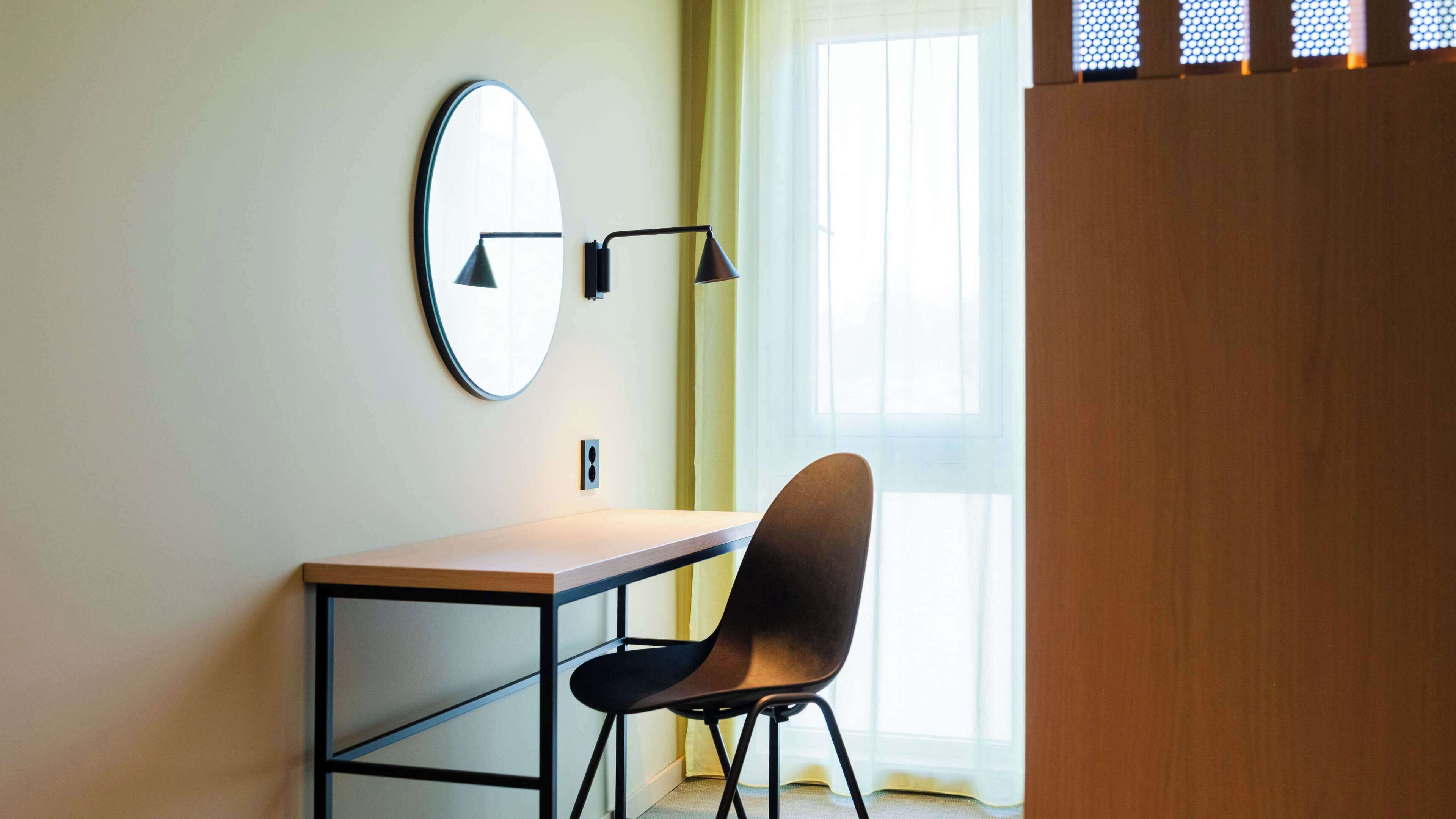 Un espacio de oficina minimalista con un escritorio, una silla, un espejo redondo y una lámpara de pie.