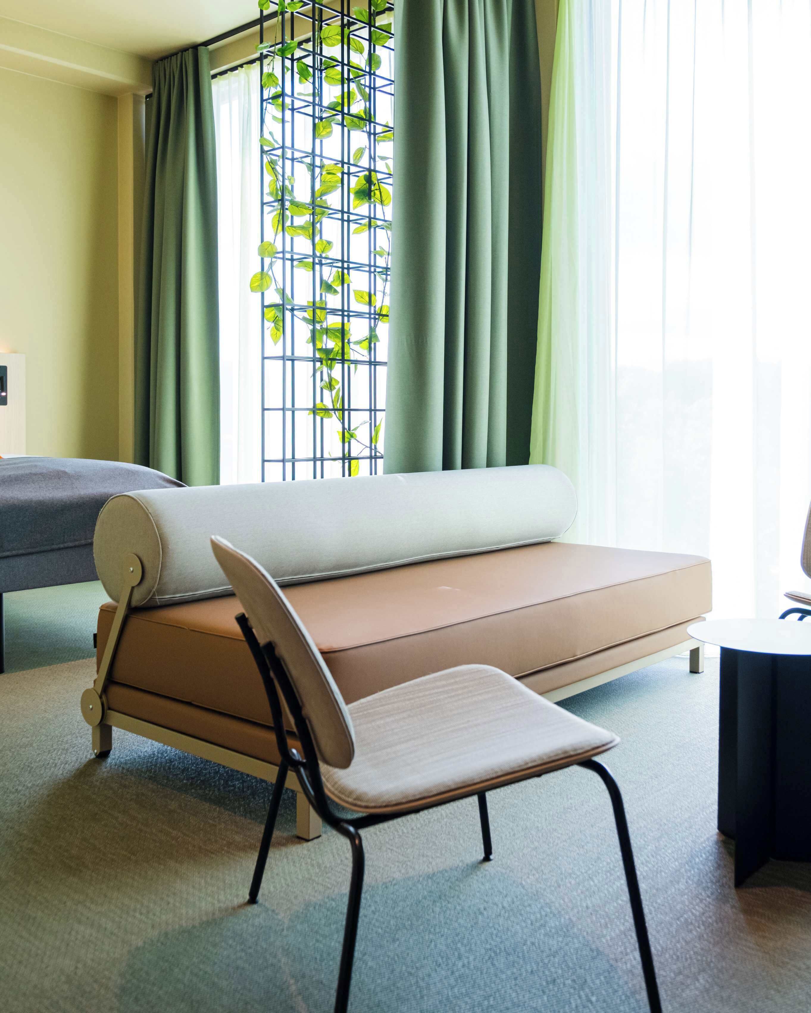 A modern room with a sofa bed, a chair, and a window with curtains.
