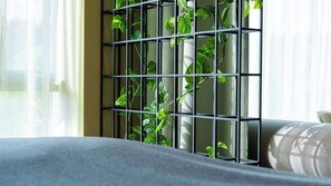 A room with a grey sofa, a black metal plant holder with green plants, and sheer curtains. - Citybox Kristiansand (Kristiansand)
