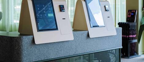 A reception area with two CityBox kiosks for check-in and check-out, a digital sign above the reception desk, and a CityBox mat on the floor.