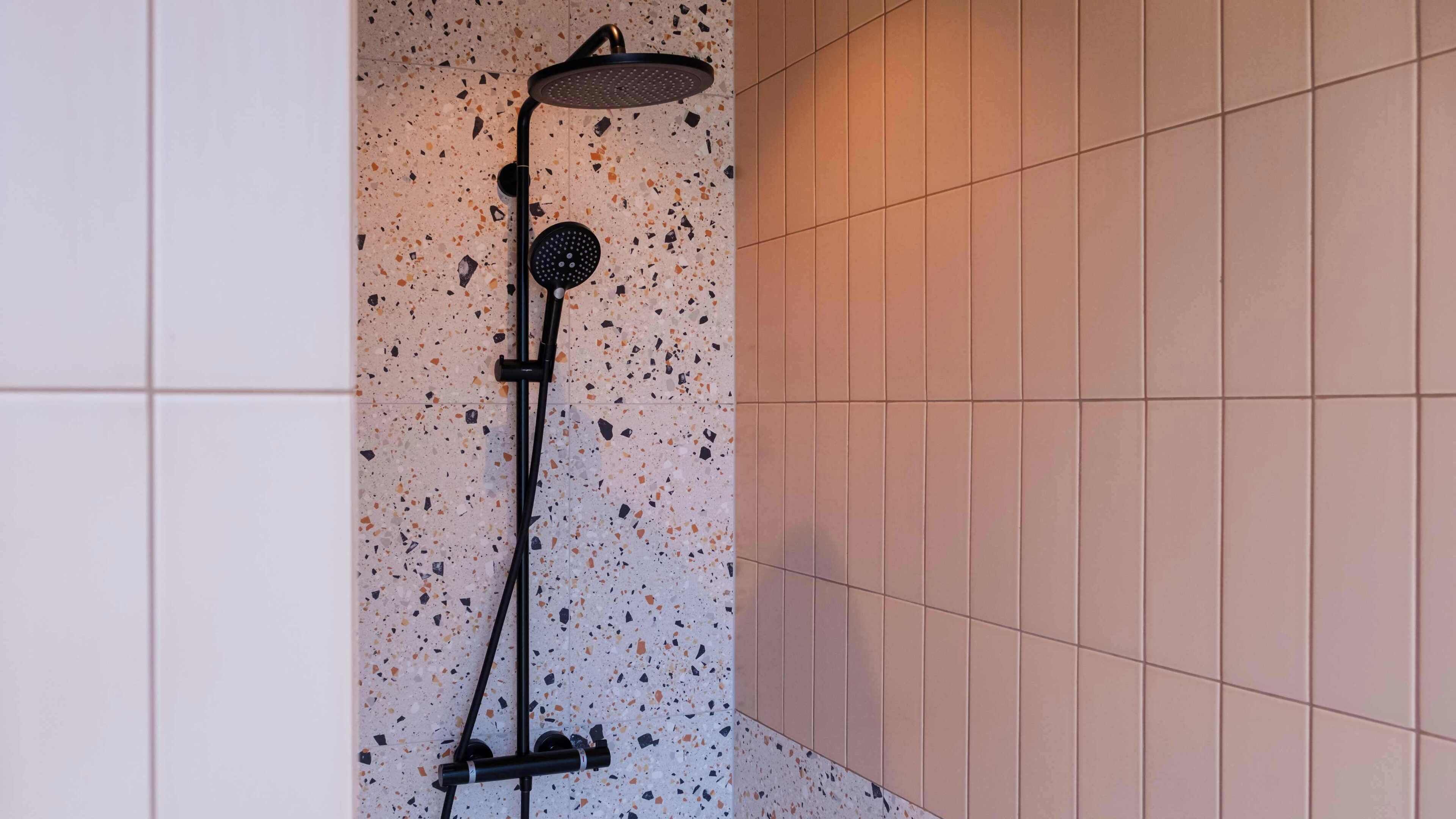 Ducha con cabezal de lluvia y alcachofa, frente a una pared de azulejos con salpicaduras.