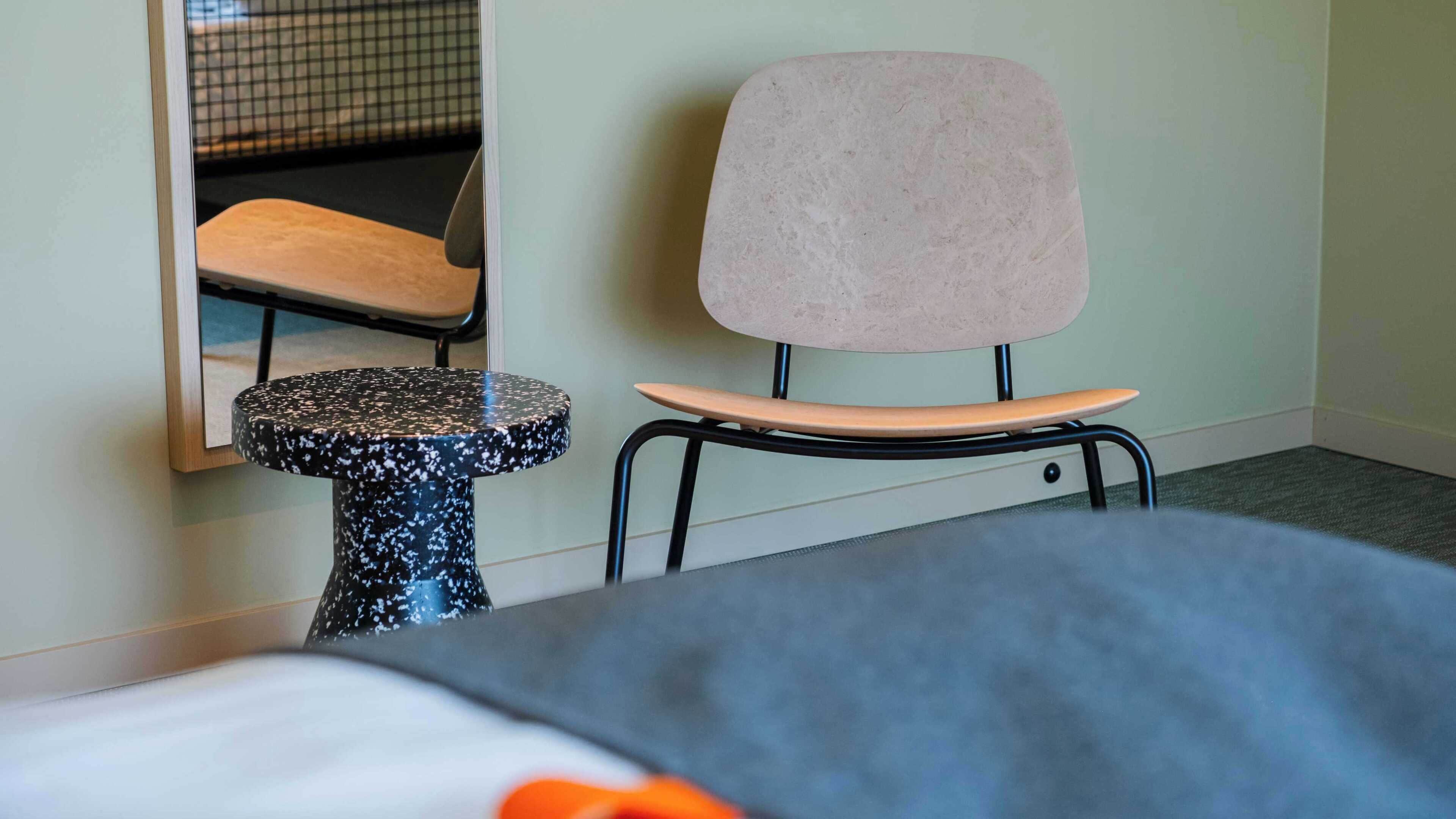 A hotel room with a bed, a small round table, a chair, and a mirror on the wall.