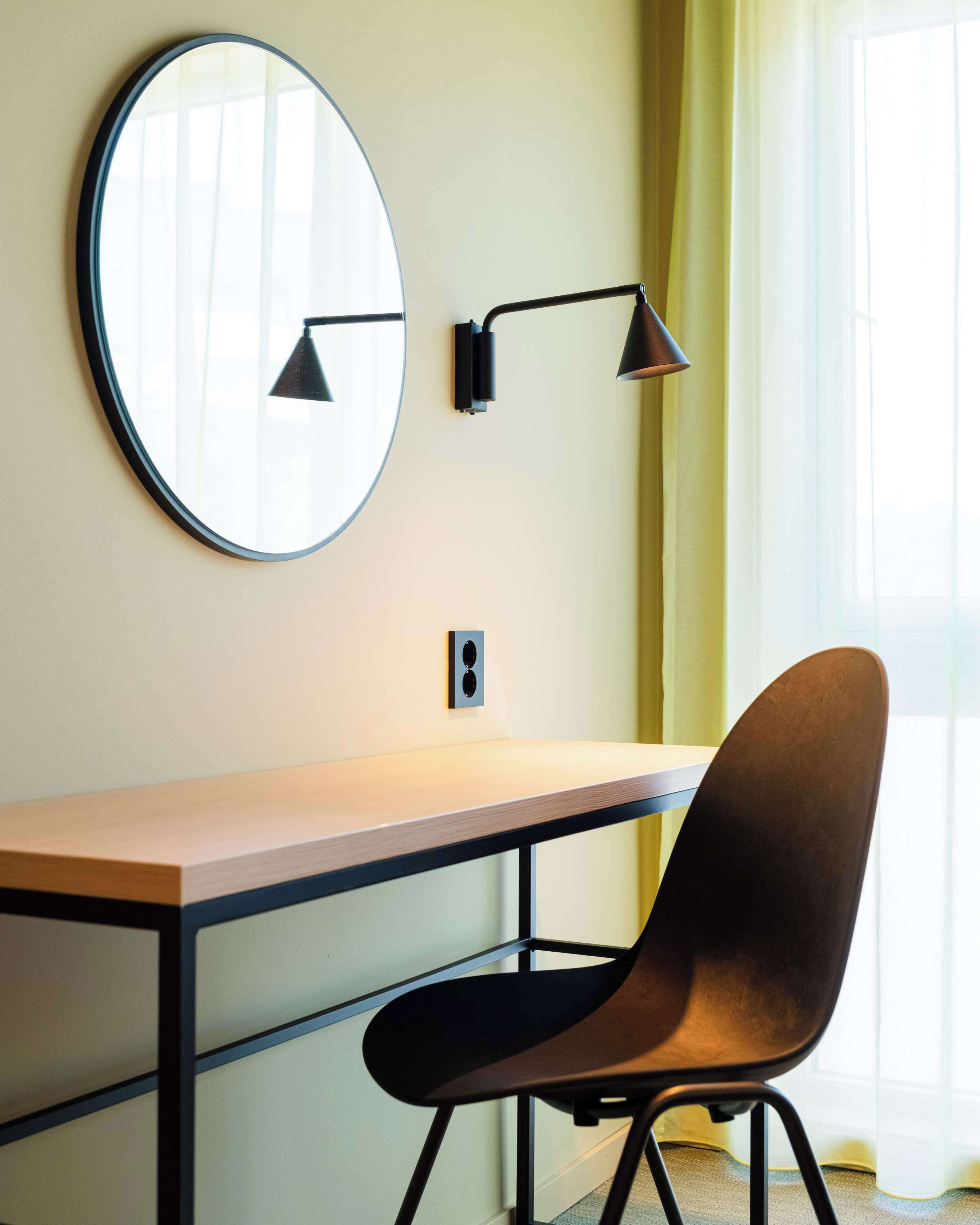 Ein modernes Zimmer mit Schreibtisch, Stuhl, rundem Spiegel und zwei Wandlampen.