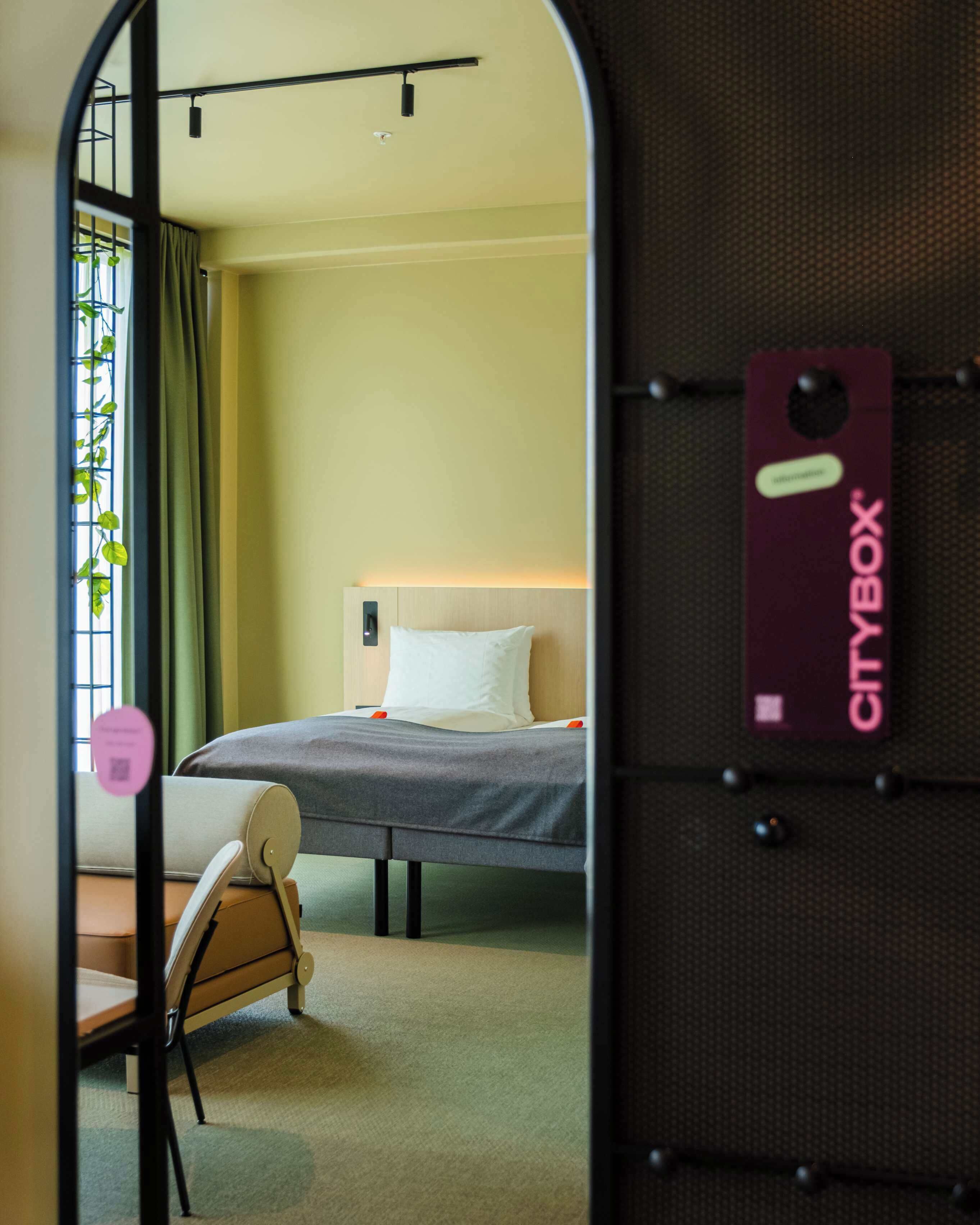 A hotel room with a bed, a chair, a desk, and a window with curtains.