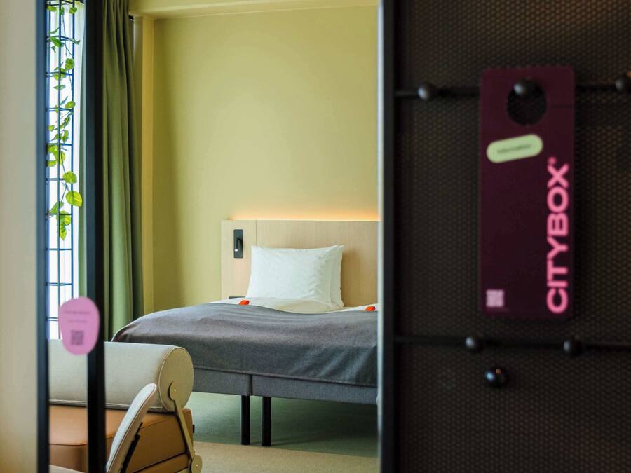 Ein Hotelzimmer mit Bett, Stuhl, Schreibtisch und einem Fenster mit Vorhängen.